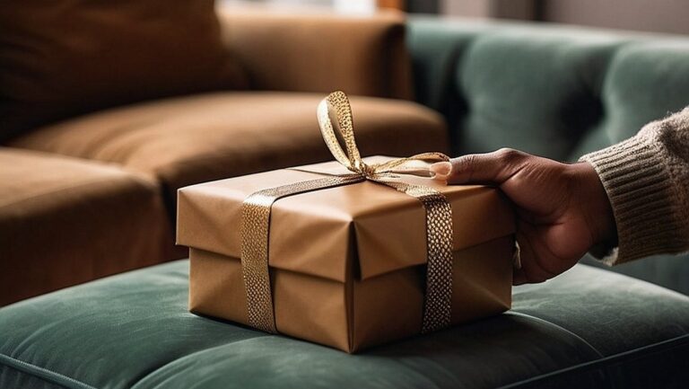 Vyriška ranka, laikanti dailaus ir modernaus dizaino dovanų dėžutę. Fone – šilta ir jauki svetainė, dekoruota subtiliais vyriškumo potėpiais.