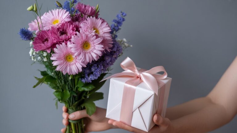 Realistiškas kadras: ranka švelniai laikanti gyvybingą, rasus šviežių gėlių puokštę ir gražiai suvyniotą dovanų dėžutę, siūlančią apgalvotą pristatymą.