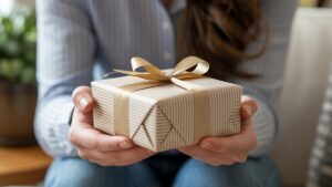 Realistiškas, iš arti: žmogaus rankos mandagiai gauna apgalvotai suvyniotą dovaną, subtilią, vertinamą šypseną, užsimenančią apie rafinuotą etiketą ir pageidavimus.