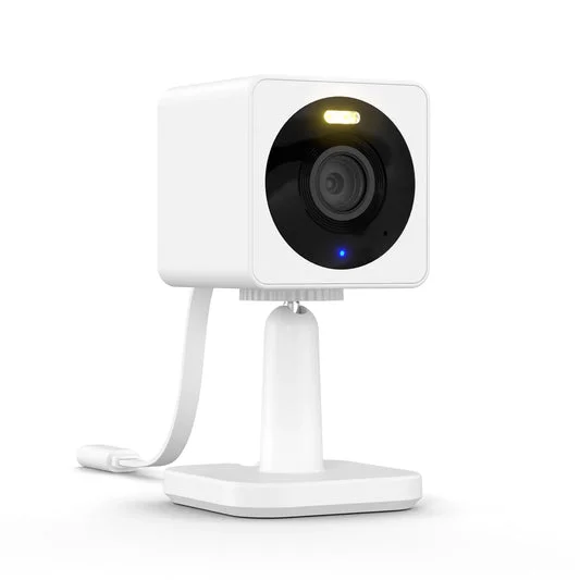 Wyze Cam v3, a compact white cube-shaped security camera, shown on a table with its stand, emphasizing its small footprint.